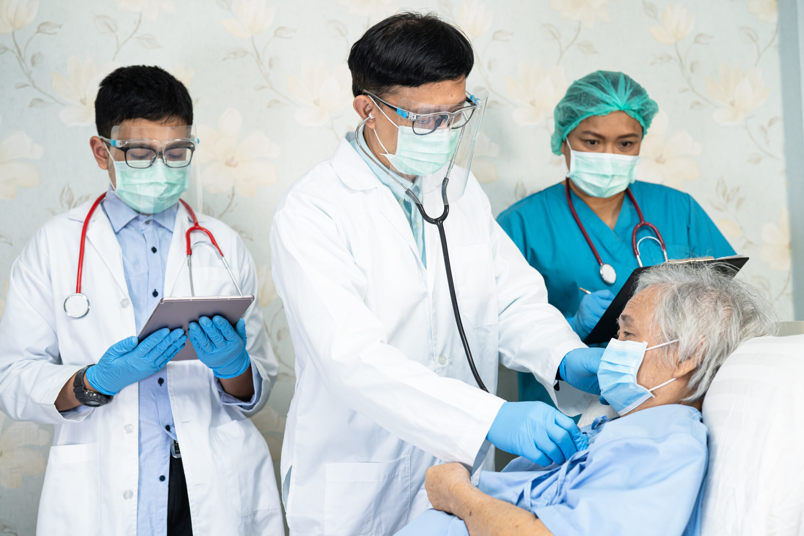 Asian doctor team check old senior lady patient for disease to motivation new normal to treat infection Covid-19 Coronavirus at hospital ward.