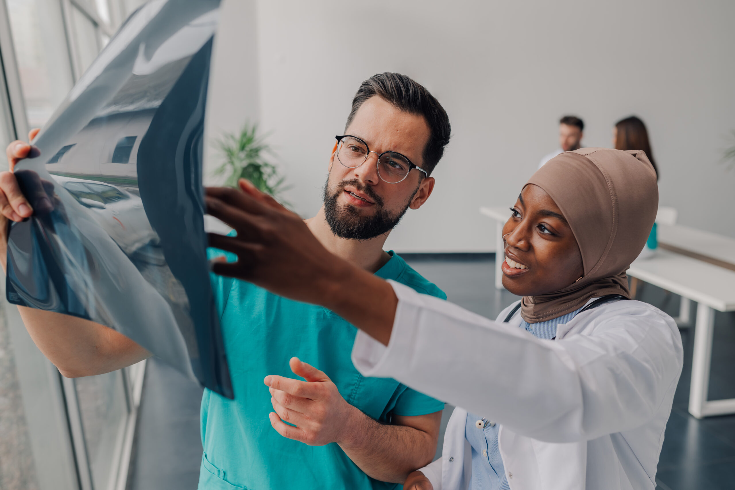Two diverse doctors, a male and a female wearing hijab, are carefully examining an x ray image in a modern hospital setting, collaborating on a diagnosis