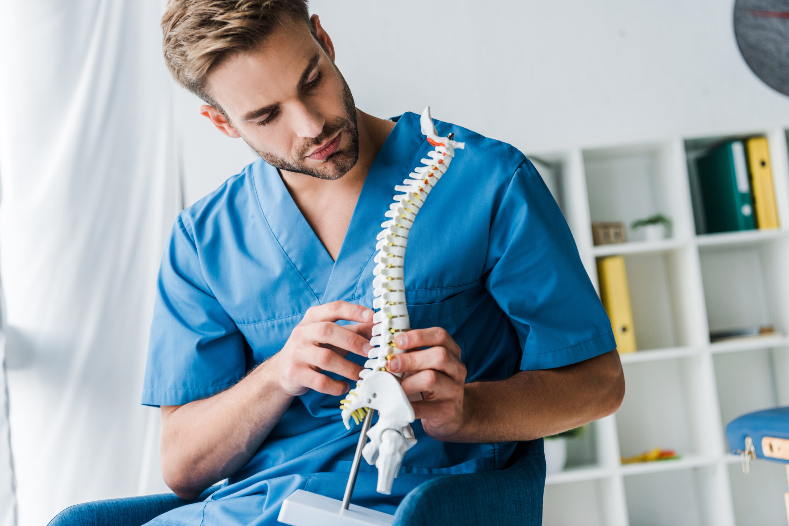 bearded doctor touching spine model while sitting in armchair