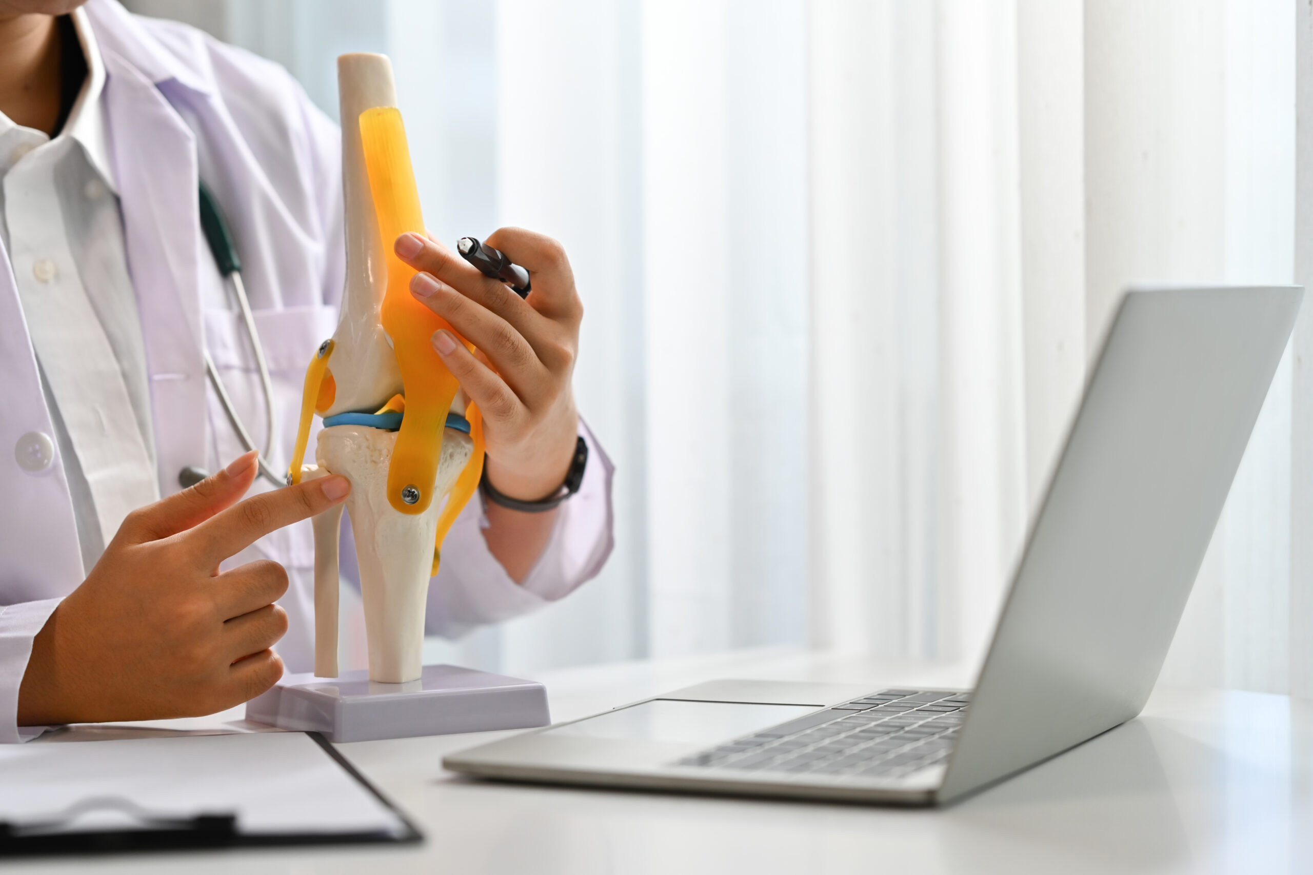 Orthopedist or traumatologist with knee joint model having online consultation on laptop. Telemedicine and healthcare.