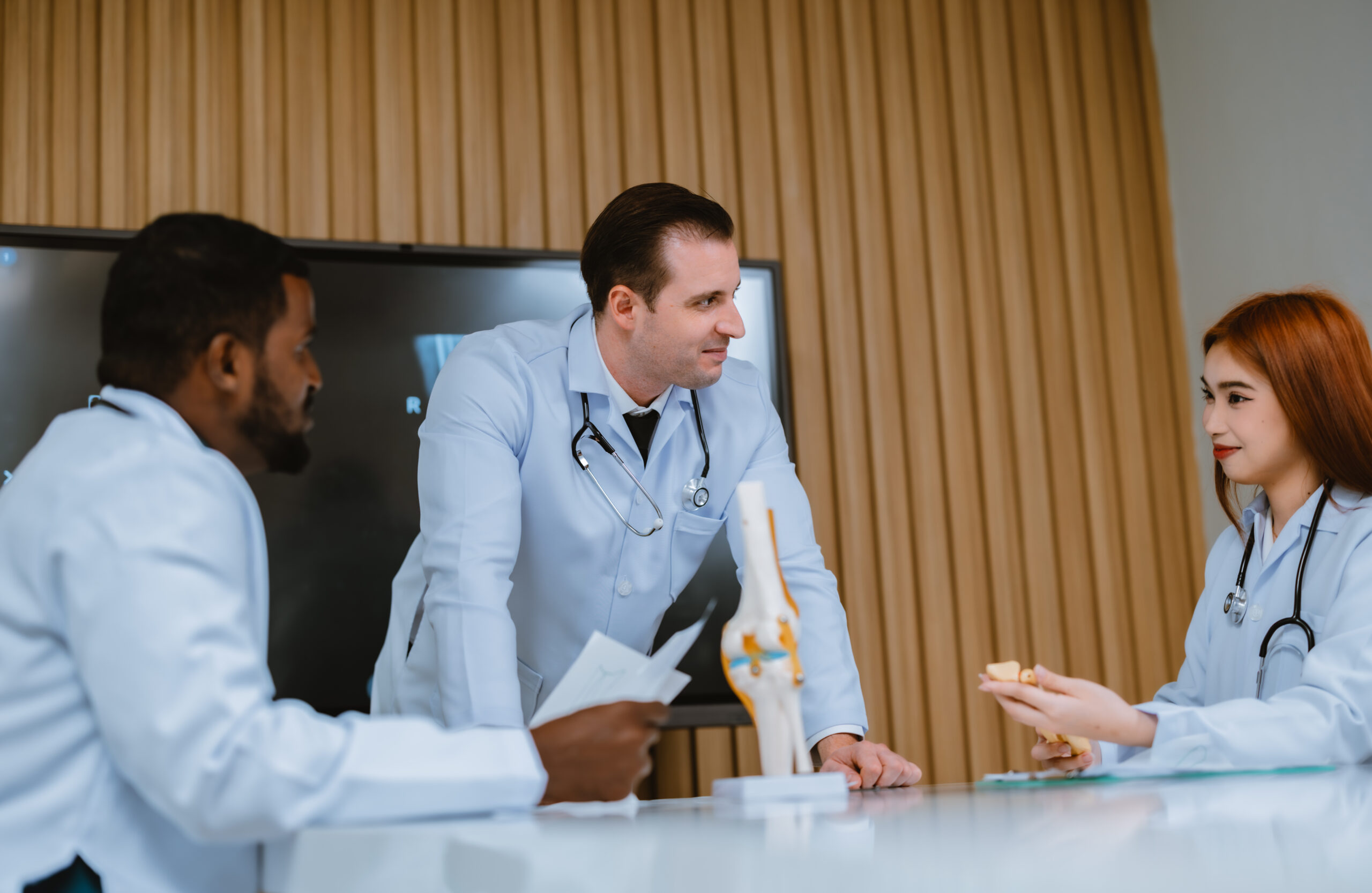 A multicultural boardroom discussion between the surgeon, radiologist on patient's case of ankle injuries. They examine, analyze MRI scans for the most effective, precise treatment plan and procedure