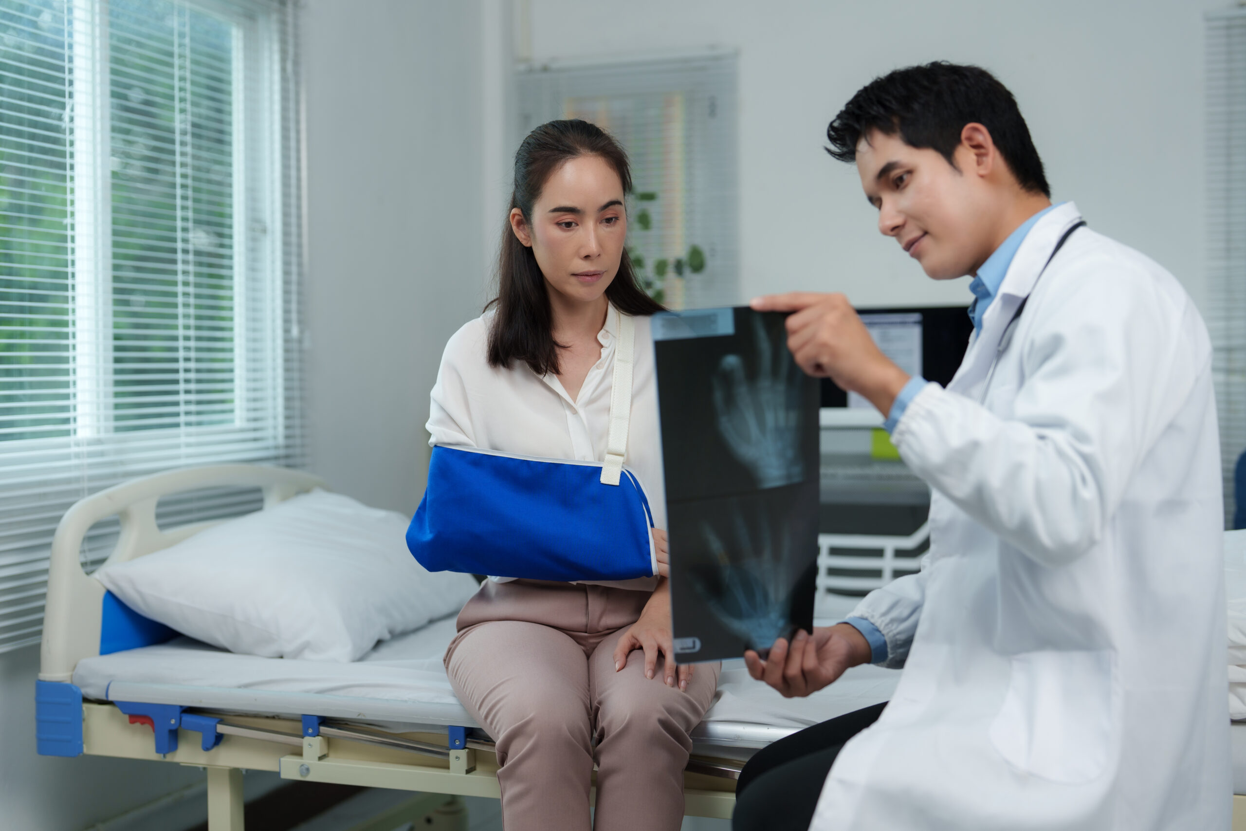 Doctor explaining radiography to a patient with broken arm wearing an arm sling