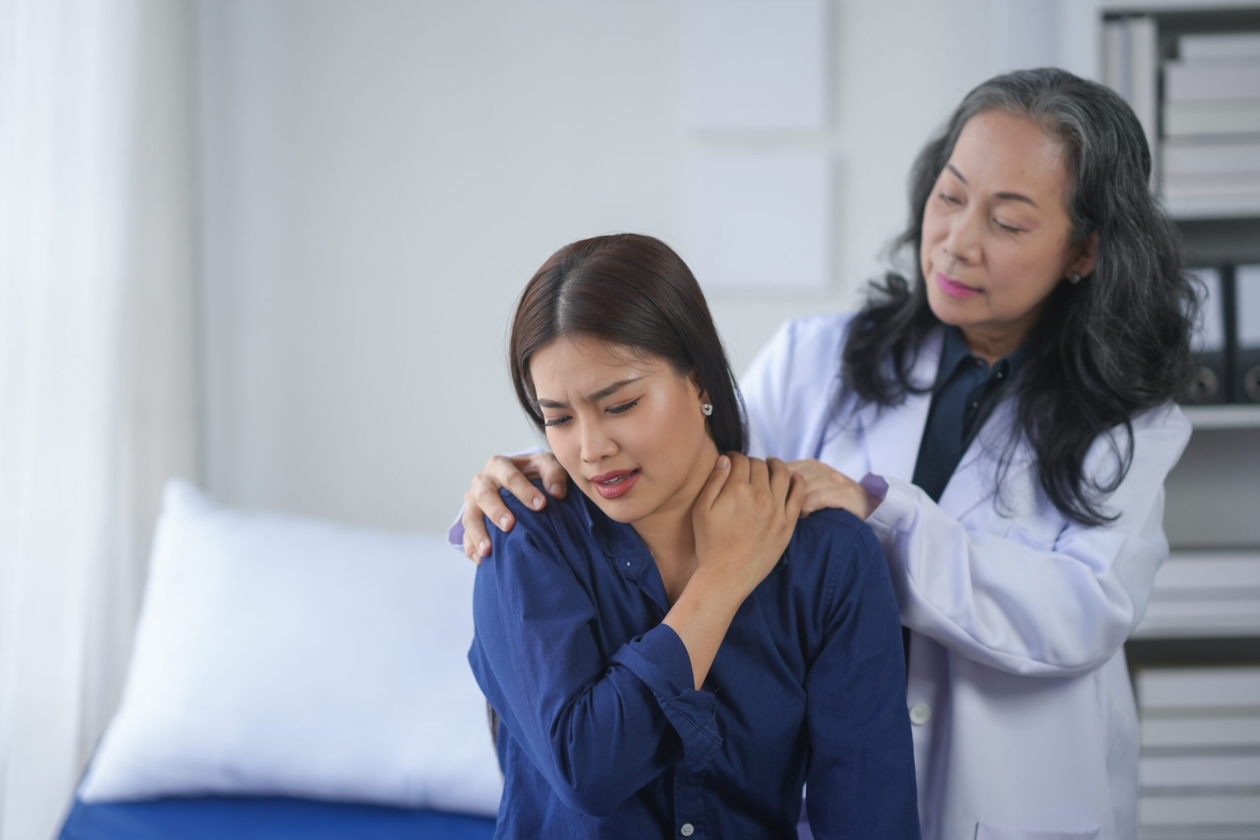 A healthcare professional assists a patient experiencing shoulder pain in a bright, modern medical office.