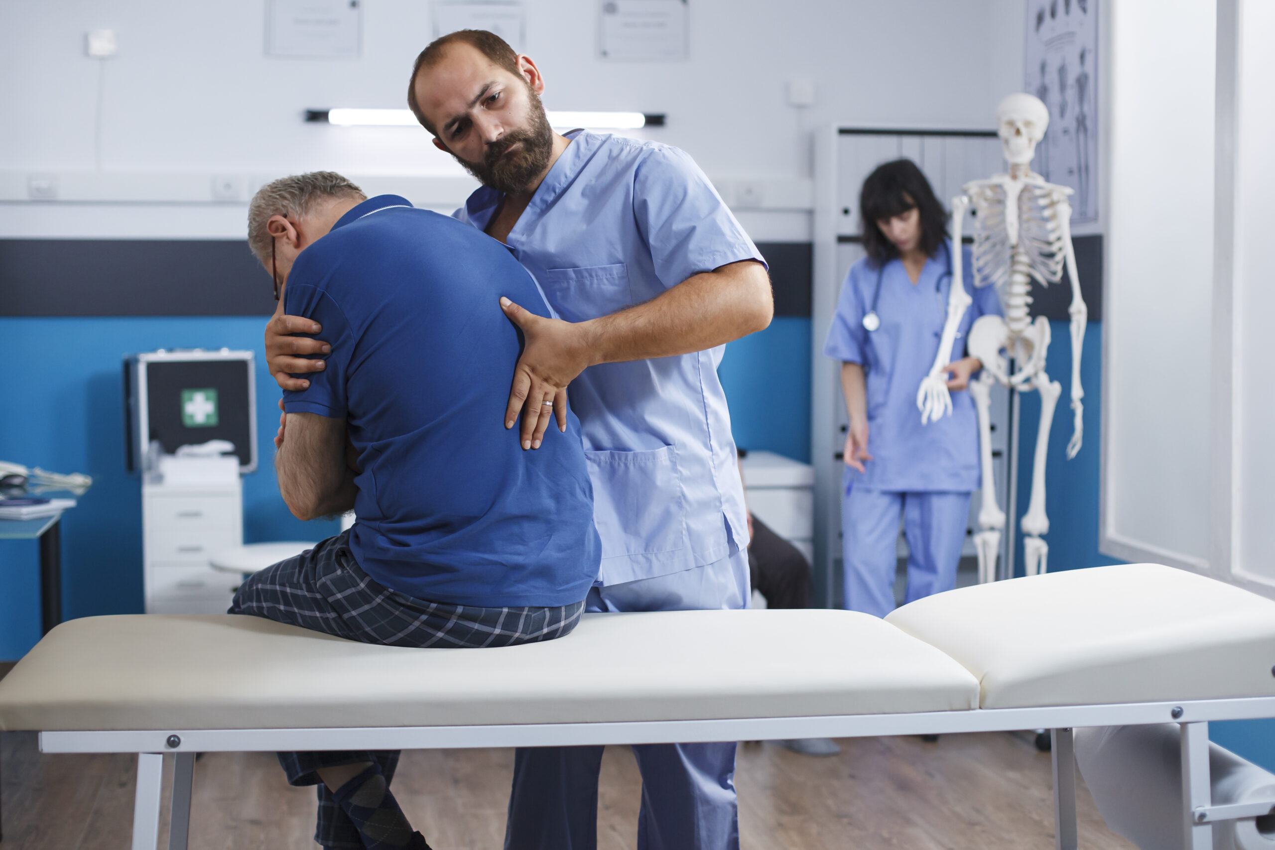 Osteopathic nurse gently extends spine of elderly patient with injury as part of physiotherapy. Chiropractor provides aid to gentleman experiencing back pains, aiding in physical recovery.