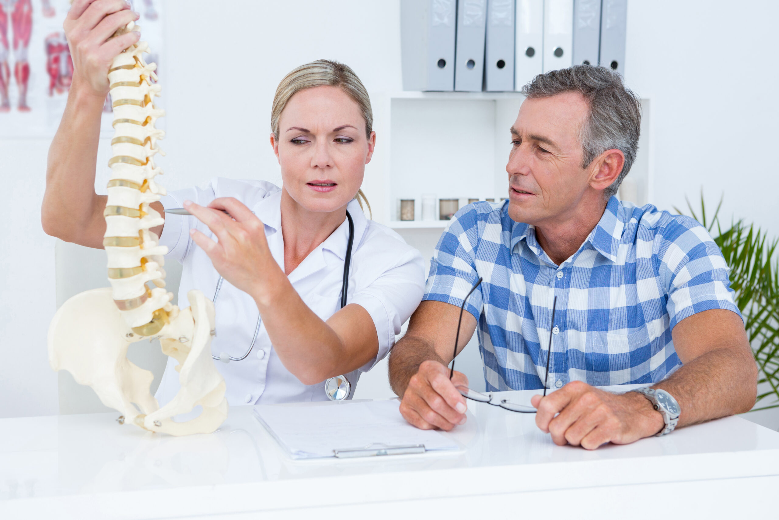Doctor showing anatomical spine to her patient in medical office