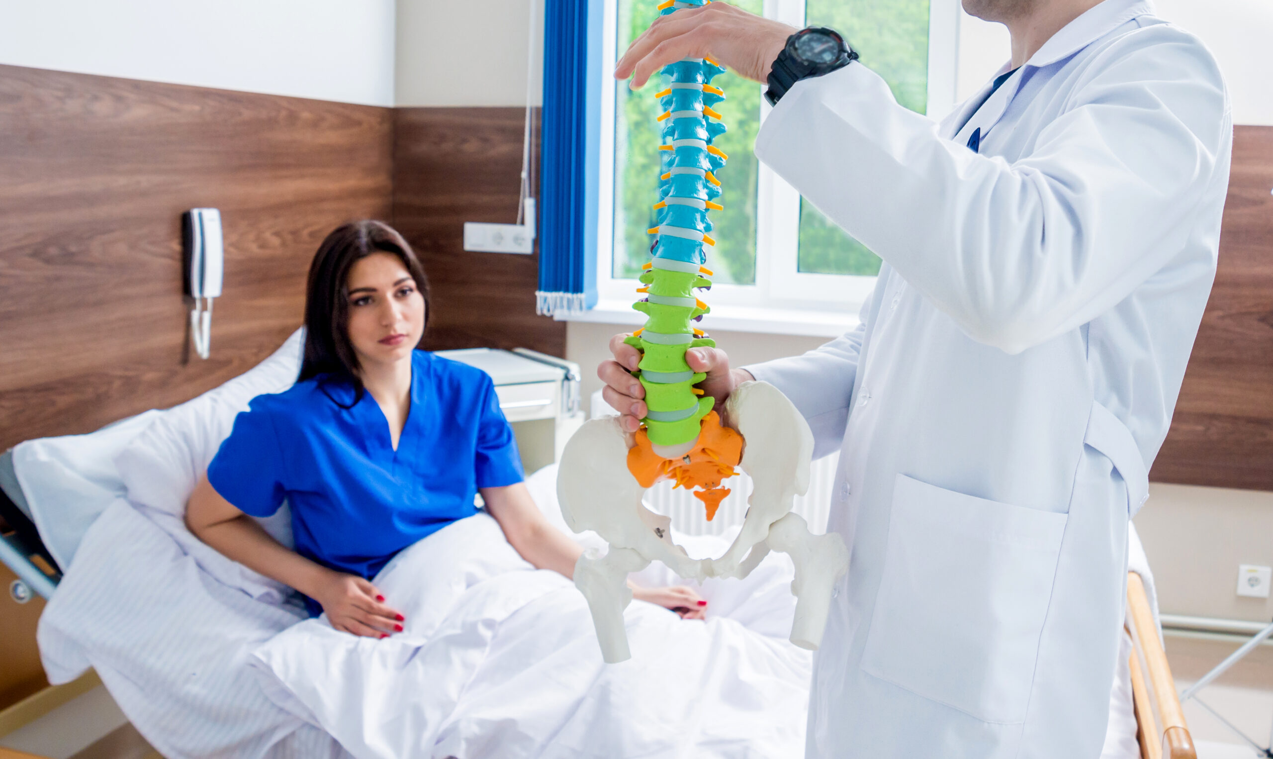 Orthopedist showing spine model to patient in hospital. Medical background