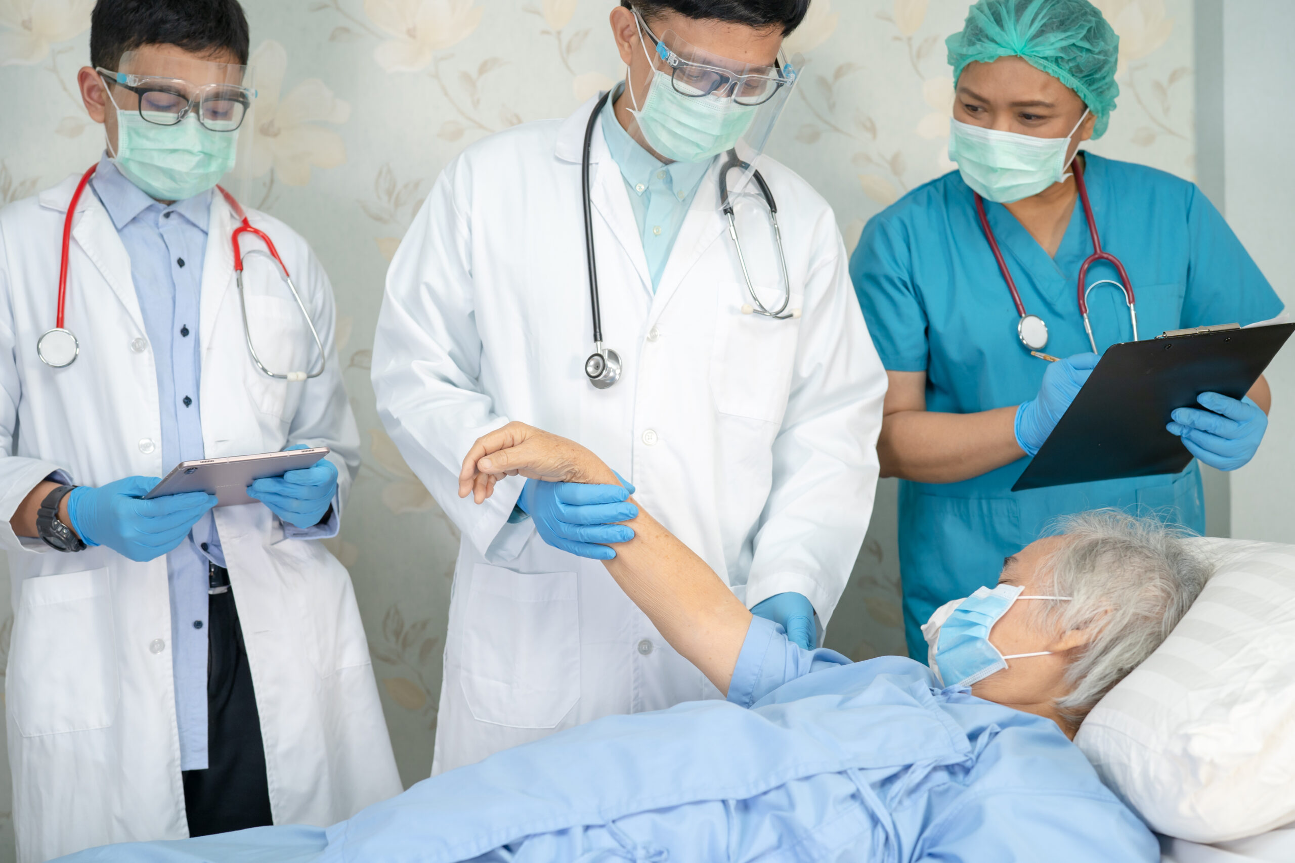 Asian doctor team check old senior lady patient for disease to motivation new normal to treat infection Covid-19 Coronavirus at hospital ward.