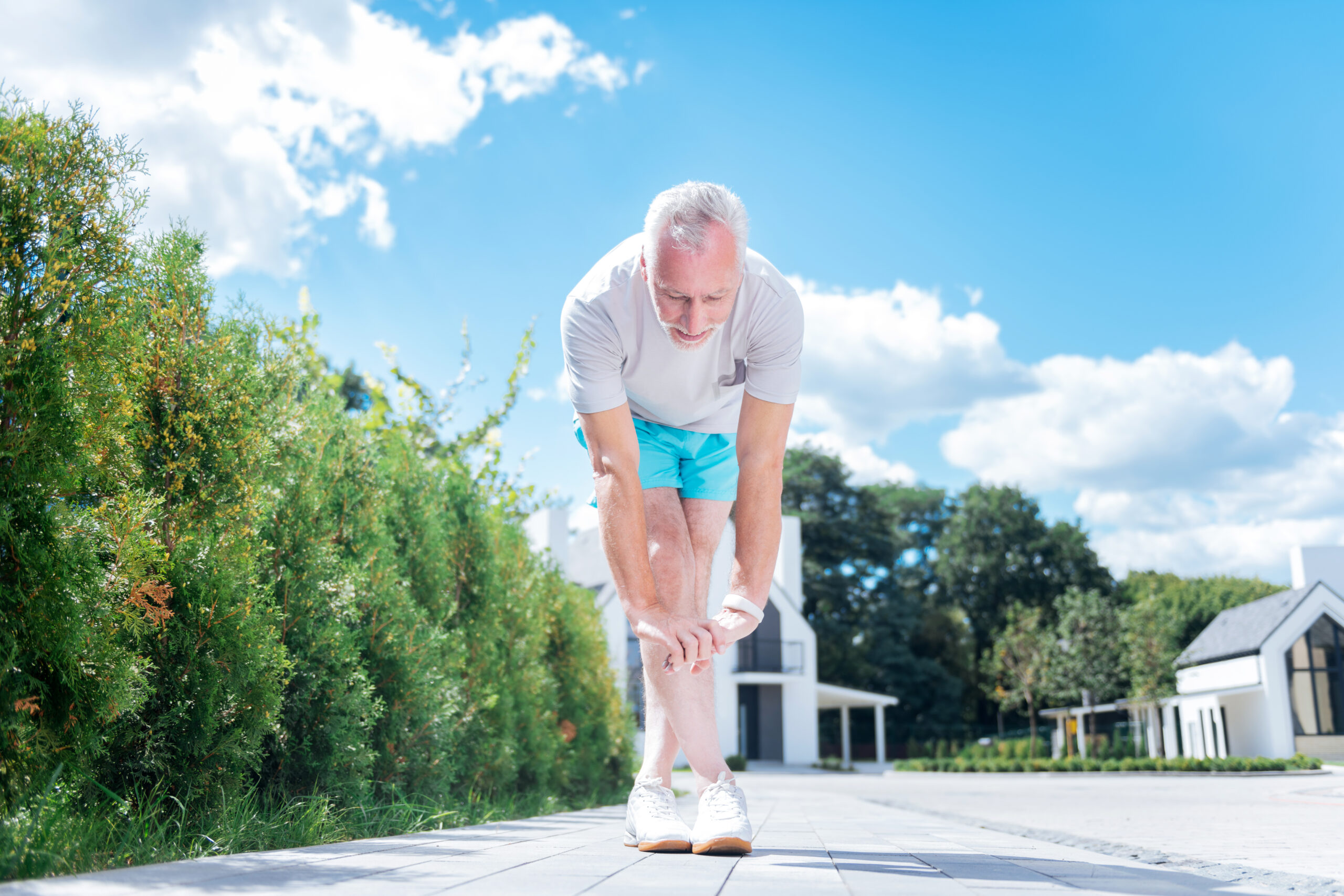 Businessman stretching. Bearded mature businessman wearing blue shorts and white sneakers stretching legs after morning run
