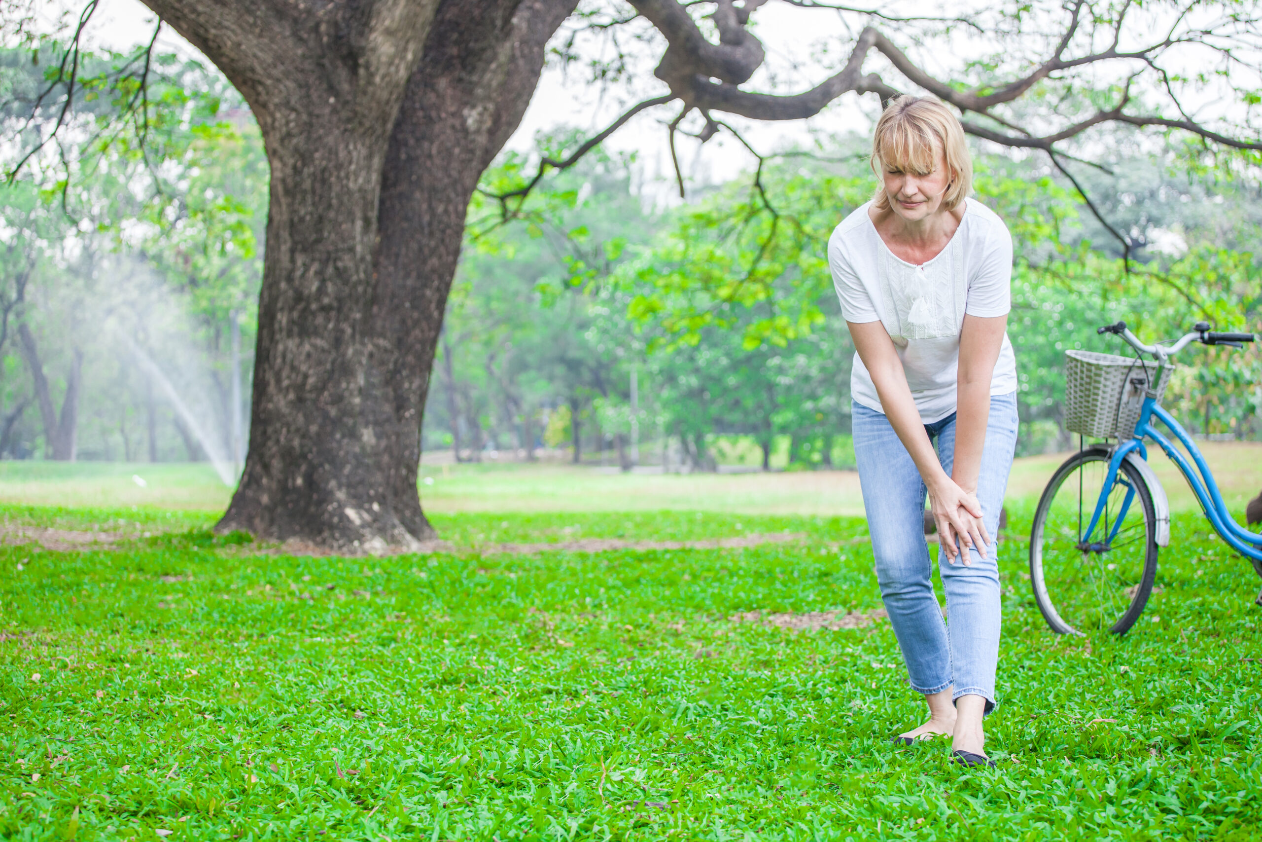 Senior woman walking in autumn park and having knee pain. Arthritis pain concept.